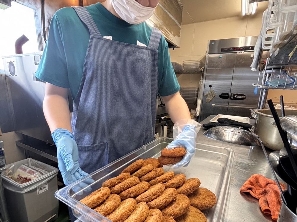 揚げ上がったメンチカツをバットに並べるスタッフ